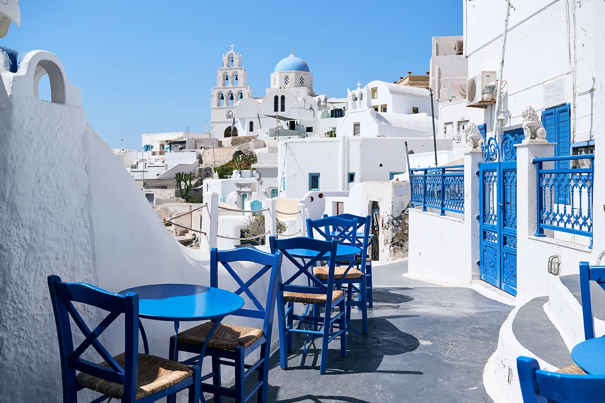Rue typique avec des tables et des chaises bleues parmi les maisons blanches du village de Pyrgos, Santorin, Grèce